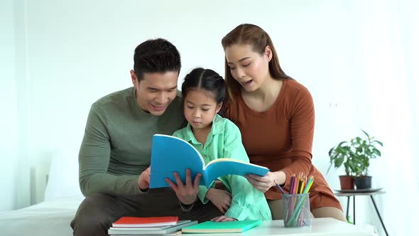Asian father and mother reading book with daughter