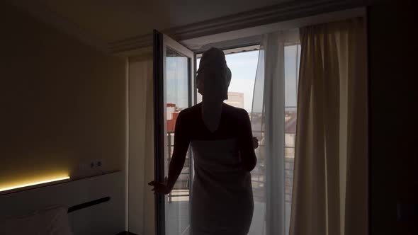 Woman in a Towel After a Bath is Standing Next to an Open Door on the Balcony