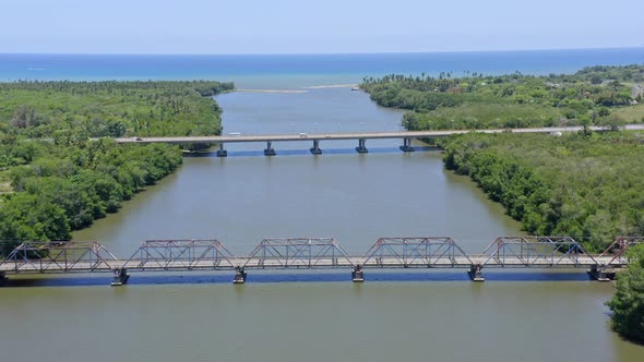 Aerial flyover cars driving on bridge over Rio Soco River and turquoise Caribbean Sea in backdrop