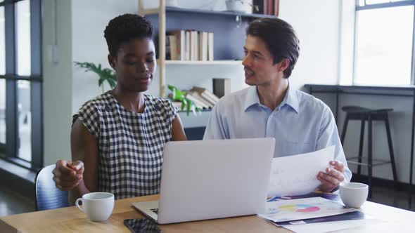 Diverse business colleagues sitting at desk using laptop going through paperwork in office