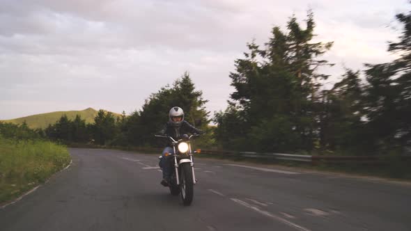 Man Riding Motorcycle on Winding Road with Green Hills