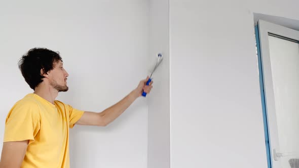 A Man Wearing a Yellow Tshirt Paints the Wall Using a Roller Painter