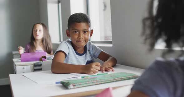 Video of happy biracial boy sitting at desk in classsroom alt