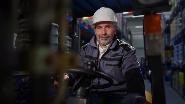 Senior Bearded Caucasian Man Sitting in Forklift Turning Off Equipment Looking at Camera Smiling
