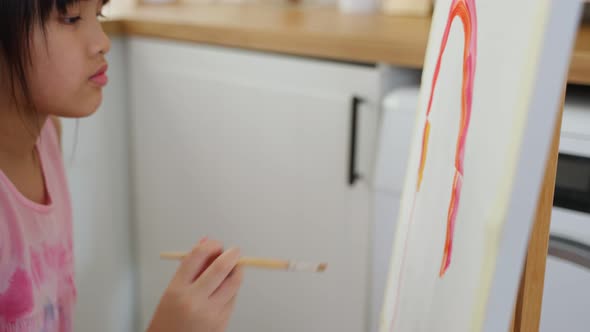 Asian young happy kid girl coloring on painting board in living room.