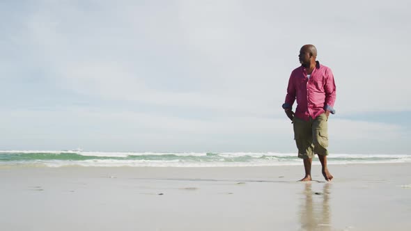 African american senior man walking on a beach looking at the sea