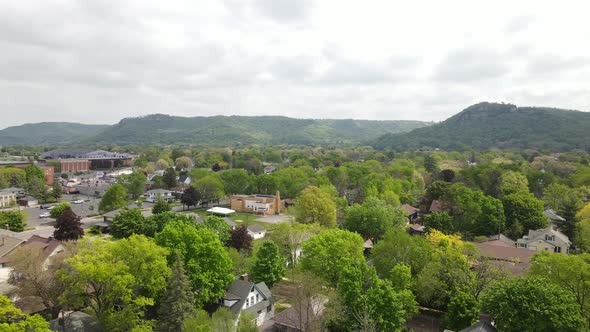 Flyover of residential neighborhood with mountain range covered in trees in Wisconsin. alt