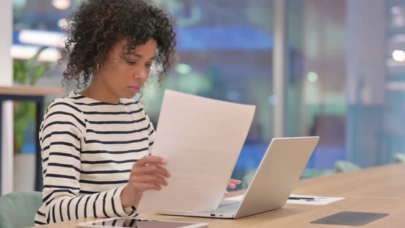 African Woman with Laptop Reading Documents in Office