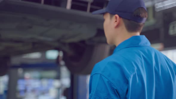 Asian automotive mechanic repairman look under car condition in garage.