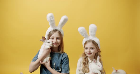 Cute Girls with Rabbit Ears Playing with the Rabbit on an Isolated Background