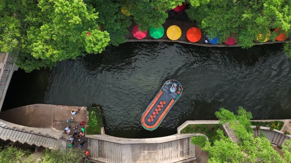 Small boat passes under bridge beside San Antonio River Walk. Famous tourist attraction. Aerial.