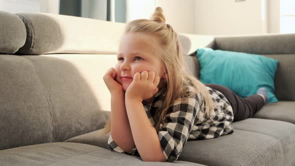Little girl child watching TV at home lying on the couch