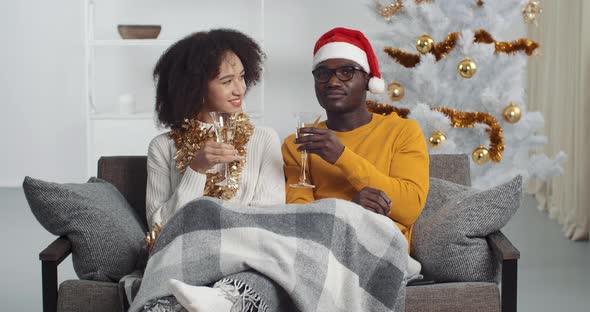 Afro American Couple Sitting Together on Sofa Under Blanket Near Christmas Tree Celebrating New Year