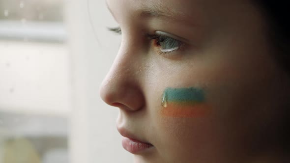 girl child at the window with the flag of ukraine on a cheek. State support in war. United Europe ag