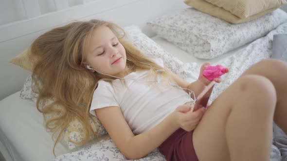 A Teenage Girl Listens to Music on Her Phone with Headphones alt