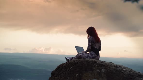 Girl Blogger Traveler is Typing Text on Laptop While Sitting on Top Mountain