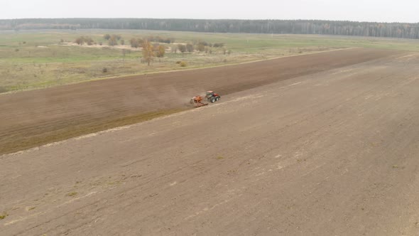 Farmer on a Tractor with a Sowing Unit Cultivates Fertile Farmland in the Spring