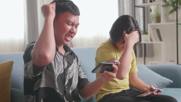 Children Playing Video Games On Mobile Phone At Home, Boy Celebrating Victory And Girl Disappointed