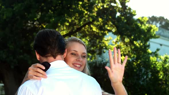 Smiling woman looking at finger ring while being embrace by man