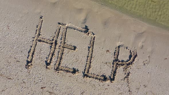 HELP written in the sand at an angle and gets smaller as aerial camera rises.