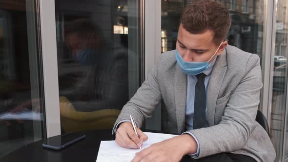 Business Man Wearing Face Mask Working with Papers in Cafe