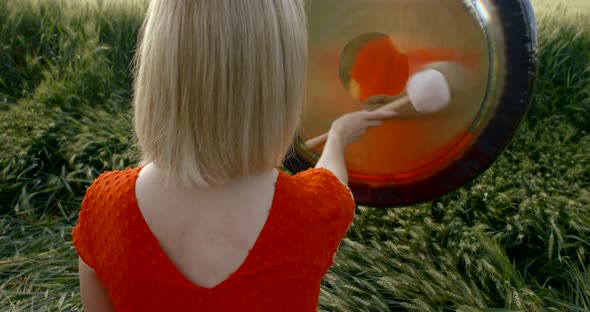 Blonde Woman Enjoys Drumming in Ethnic Drum Sitting on Field