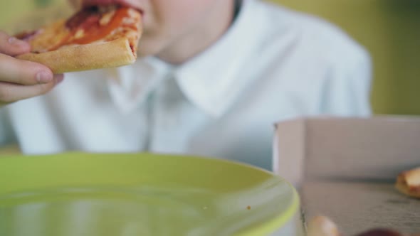 Schoolboy Eats Pizza with Tomatoes and Cheese at Table