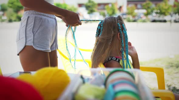 Many Threads and Ribbons Lie on the Table Against the Background of a Girl Whose African Braids are