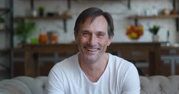 Closeup Portrait of Smiling Caucasian Mature Man Looking at Camera While Sitting at Home on Sofa