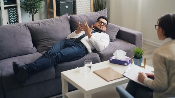 Unhappy Young Man Speaking Lying on Sofa in Psychologist's Office in Clinic