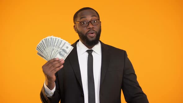 Cheerful Afro-American Man in Formalwear Pointing at Bunch of Dollar Cash, Coach
