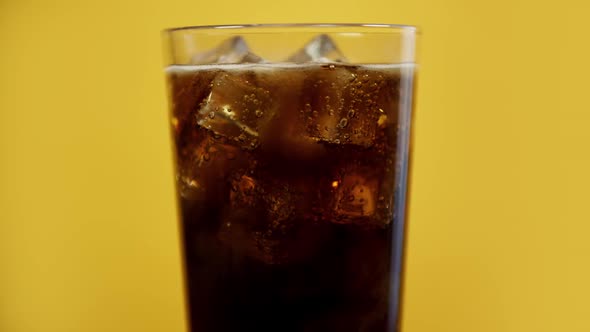 Glass Full of Cola Fizzy Drink with Ice Cubes. Cold Sparkling Soda on Yellow Background