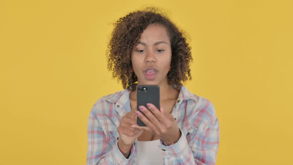 Young African Woman Celebrating on Smartphone on Yellow Background