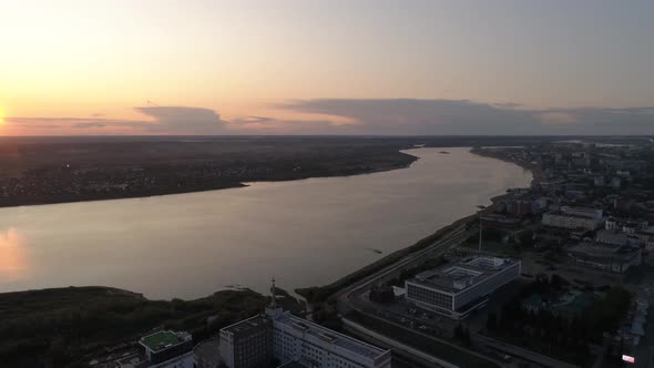 Aerial view of evening city and river at sunset. Cars drive on the roads. Summer warm evening 02