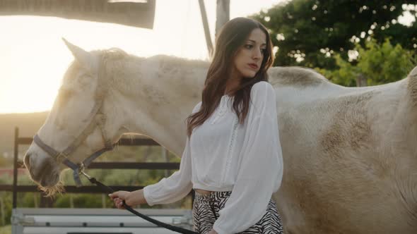 Girl Relaxes with Her White Horse in Front of the Ranch at Sunset