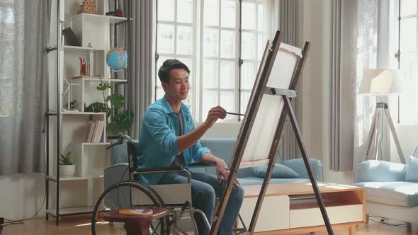 Asian Artist Man In Wheelchair Holding Paintbrush Mixed Colour And Painting On The Canvas