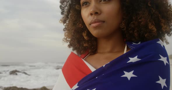 Front view of African American woman wrapped in American flag standing on the beach 4k