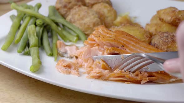 Slow Motion Slider Shot of Eating a Pan Fried Salmon Fillet on a White Plate With Vegetables