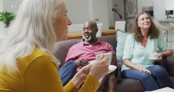 Animation of happy diverse female and male senior friends drinking coffee at home