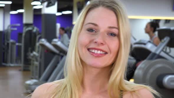 A Young Beautiful Woman Smiles at the Camera in a Gym - Face Closeup