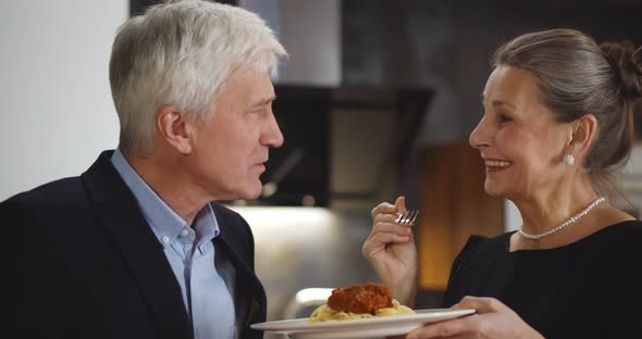 Senior Woman Feeding Husband with Delicious Pasta Having Dinner at Home