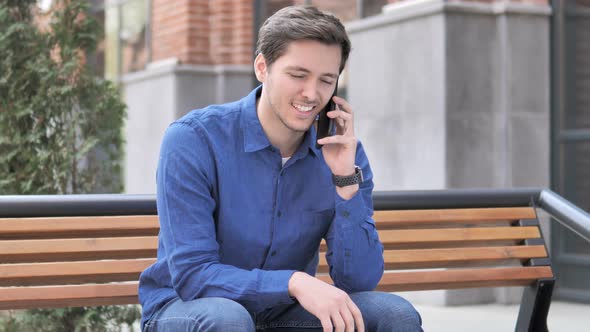 Young Man Talking on Phone, Sitting Outdoor on bench