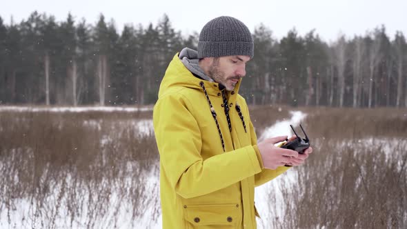 A man in a yellow jacket launches a drone in a field