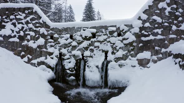 Concrete wall or dam with three spillway pipes at bottom covered in snow