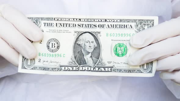 nurse or doctor is holding in one dollar bill in both hands. white gloves. corruption in medicine. 