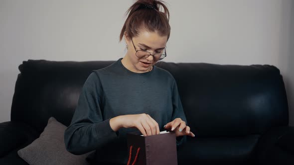 The Young Redhead with Glasses Opens the Gift and is Surprised By What She Receives