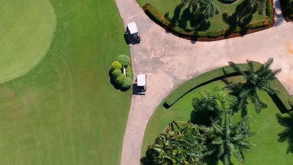 Golf buggies driving along path of lush green golf course, aerial birds eye view