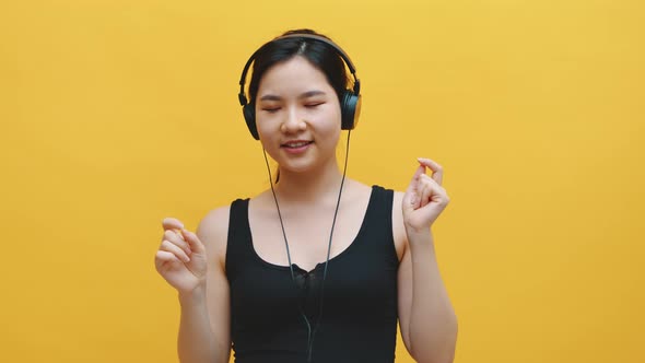 Happy Young Asian Woman with Headset Listening To the Music and Dancing. Isolated on Yellow