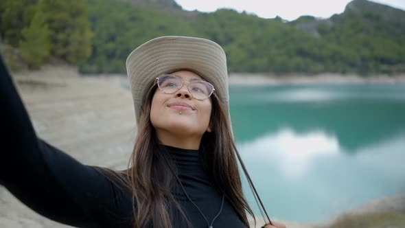 Close View of Young Woman in Hat and Glasses Taking Selfie By Lake