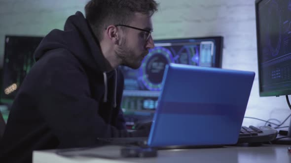 Concentrated Programmer in Eyeglasses Working with Multiple Computers and Laptop Indoors. Portrait